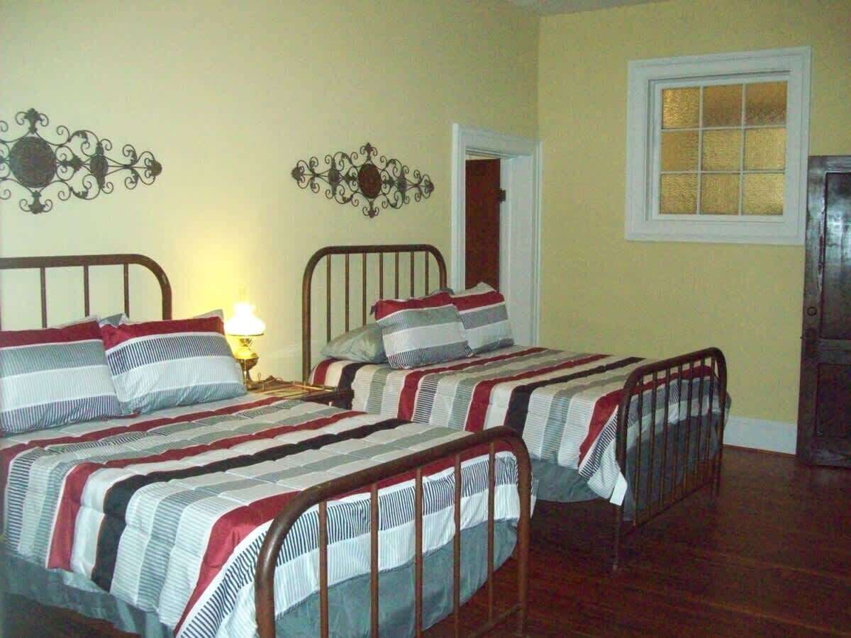 A room with two metal-framed beds, a wooden floor, a window with a white frame, and a door.
