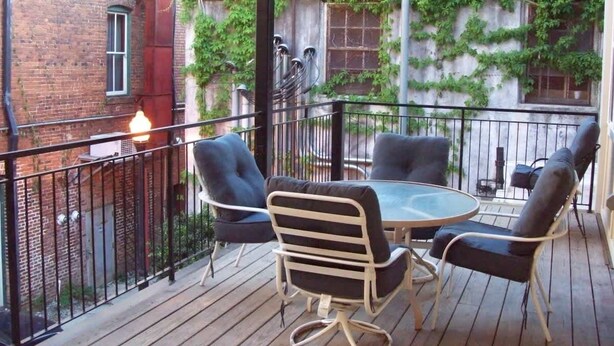 A covered outdoor seating area with a table and chairs, surrounded by a metal railing. - Large Historic Downtown Loft - Rear (Macon)