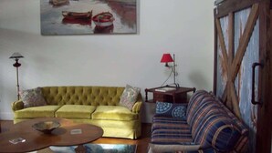 A living room with a yellow sofa, a striped sofa, a coffee table, a painting of boats, and a rustic wooden door. - Large, Unique, Ground Floor Loft with Parking #2 (Macon)