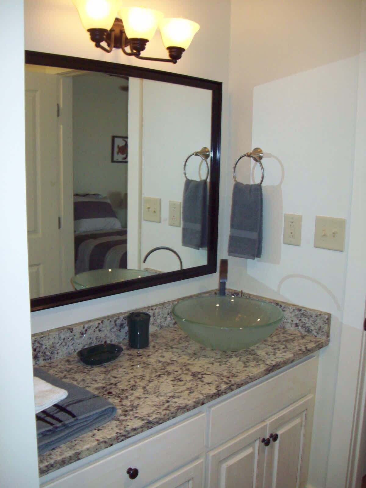 A bathroom with a large mirror, a glass sink, and a towel rack.