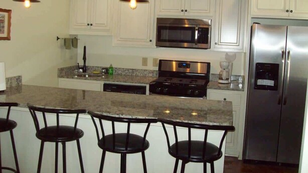 A kitchen with white cabinets, a stainless steel refrigerator, a microwave, a stove, and a bar area with stools. - Large, Unique, Ground Floor Loft with Parking #2 (Macon)