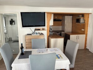 Un espace de vie compact comprenant une table à manger, des chaises, un téléviseur, un coin cuisine et une petite salle de bain.