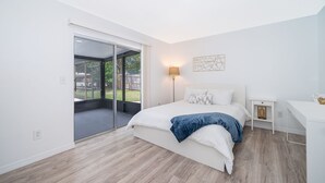 A modern bedroom with a large bed, a desk, and a sliding glass door leading to an outdoor area. - Four Season Home  (Kissimmee)