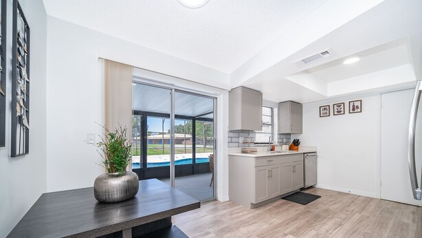A modern kitchen with a large window, sliding glass door to a pool, and a dining area with a dark wood table. - Four Season Home  (Kissimmee)