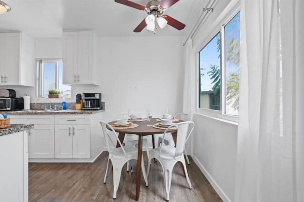 Una cocina moderna con armarios blancos, una mesa de comedor para cuatro personas y un ventilador de techo.
