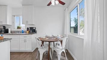 Una cocina moderna con armarios blancos, una mesa de comedor para cuatro personas y un ventilador de techo.