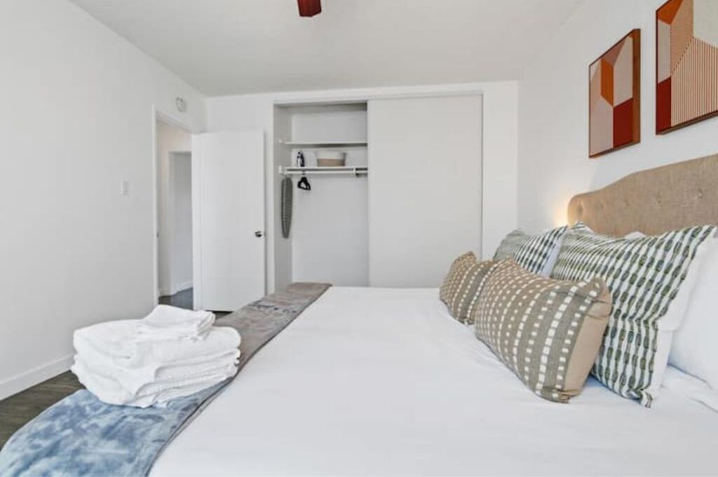 A bedroom with a bed, pillows, a bedside table, a wardrobe, and a bathroom door.