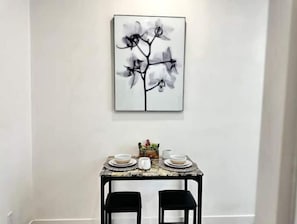 A dining area with a table set for two, featuring a marble top and black chairs.