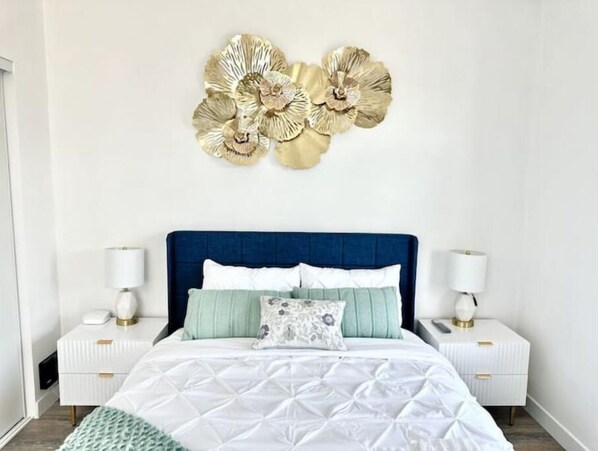A bedroom with a blue headboard, white bedding, and two bedside tables with lamps.