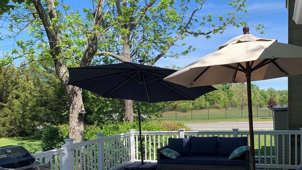 A deck with outdoor furniture, including a sofa and ottoman, under a large umbrella.