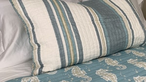 A bed with striped pillows and a blue quilt with seahorse patterns.