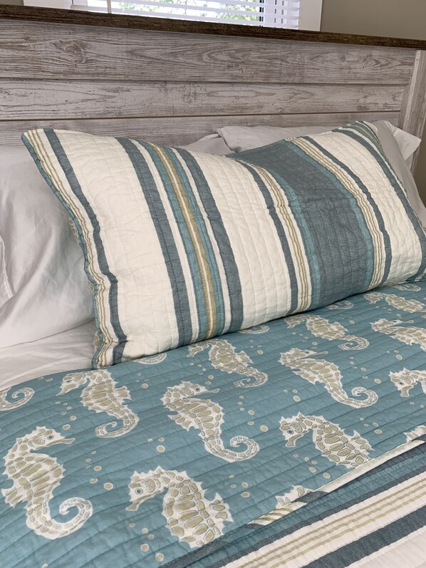 A bed with striped pillows and a blue quilt with seahorse patterns.