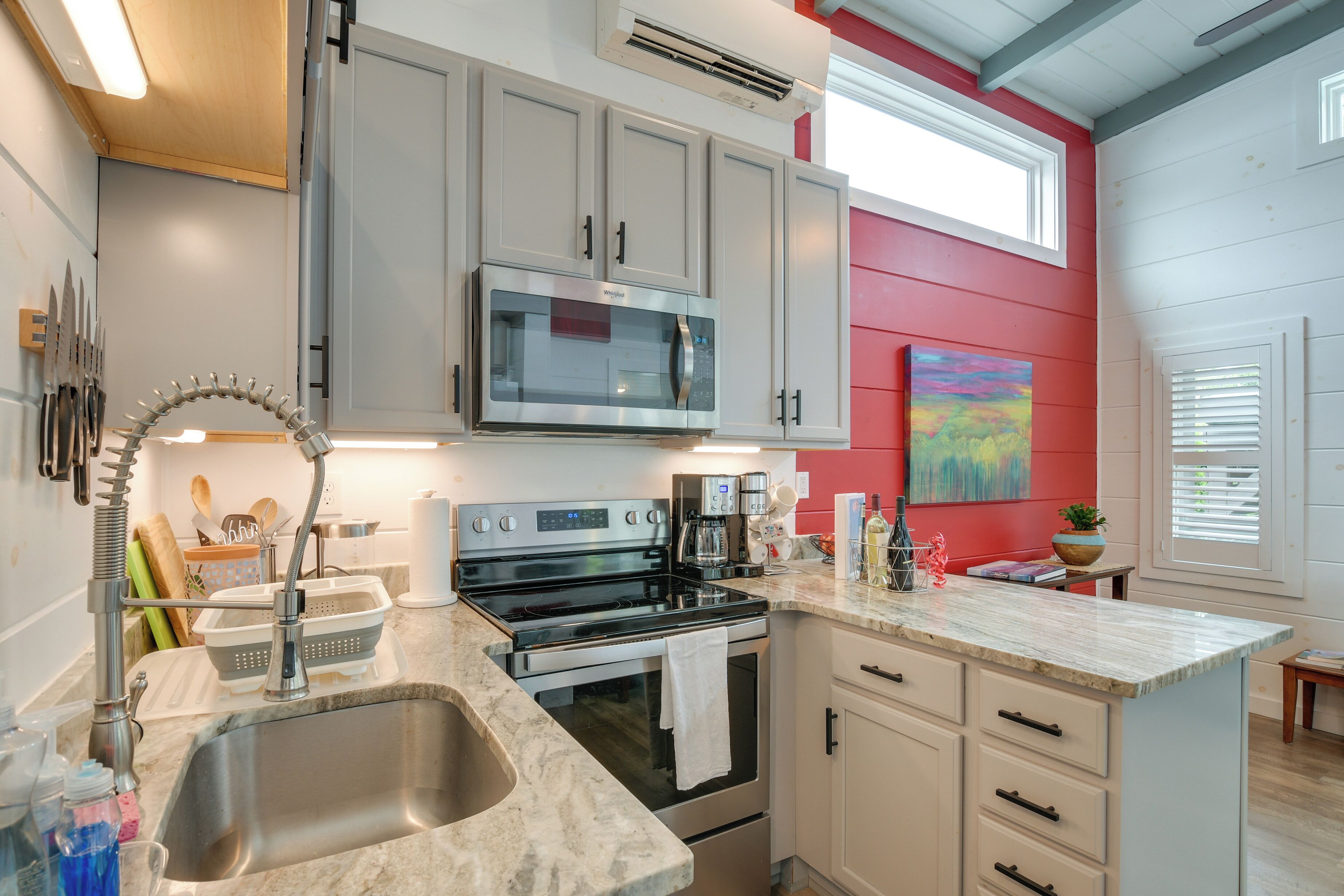 A kitchen with a stainless steel sink, a microwave, a stove, and a countertop with various items.