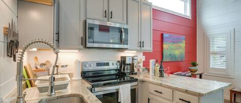 A kitchen with a stainless steel sink, a microwave, a stove, and a countertop with various items.