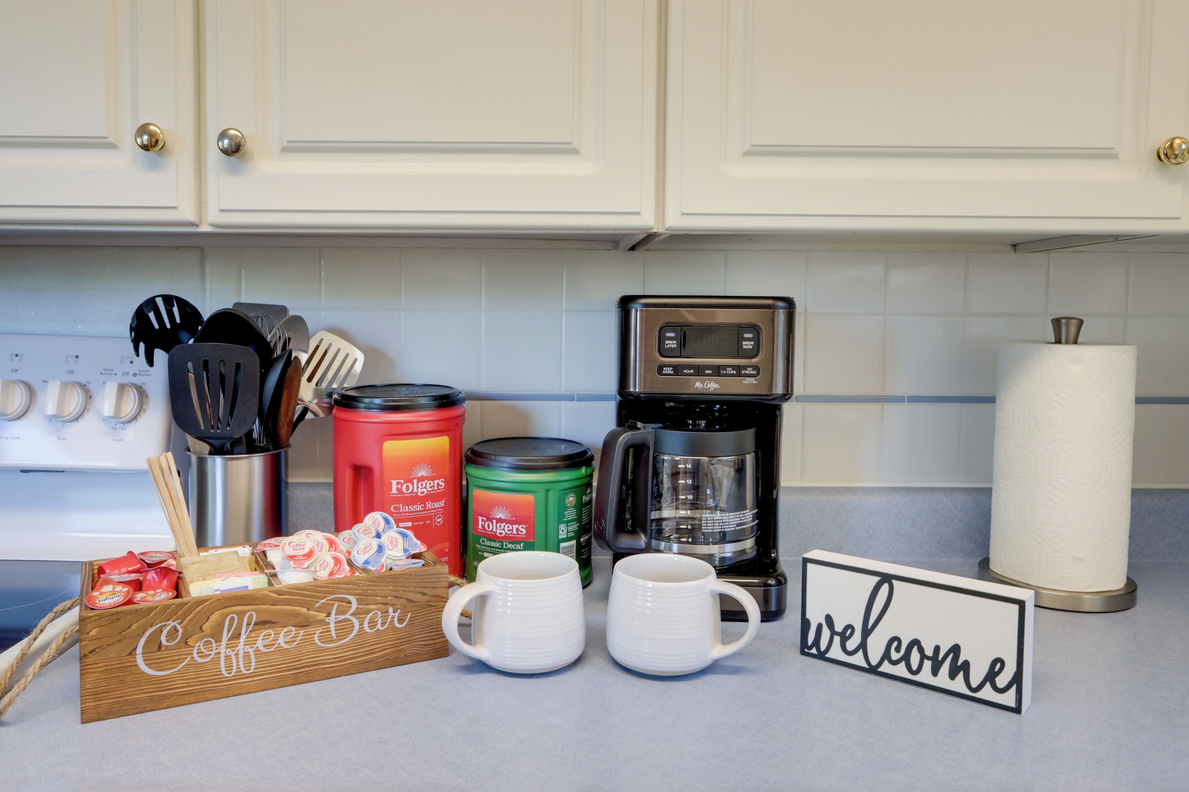 A kitchen counter with a coffee bar setup, including mugs, Folgers coffee, and a coffee maker.
