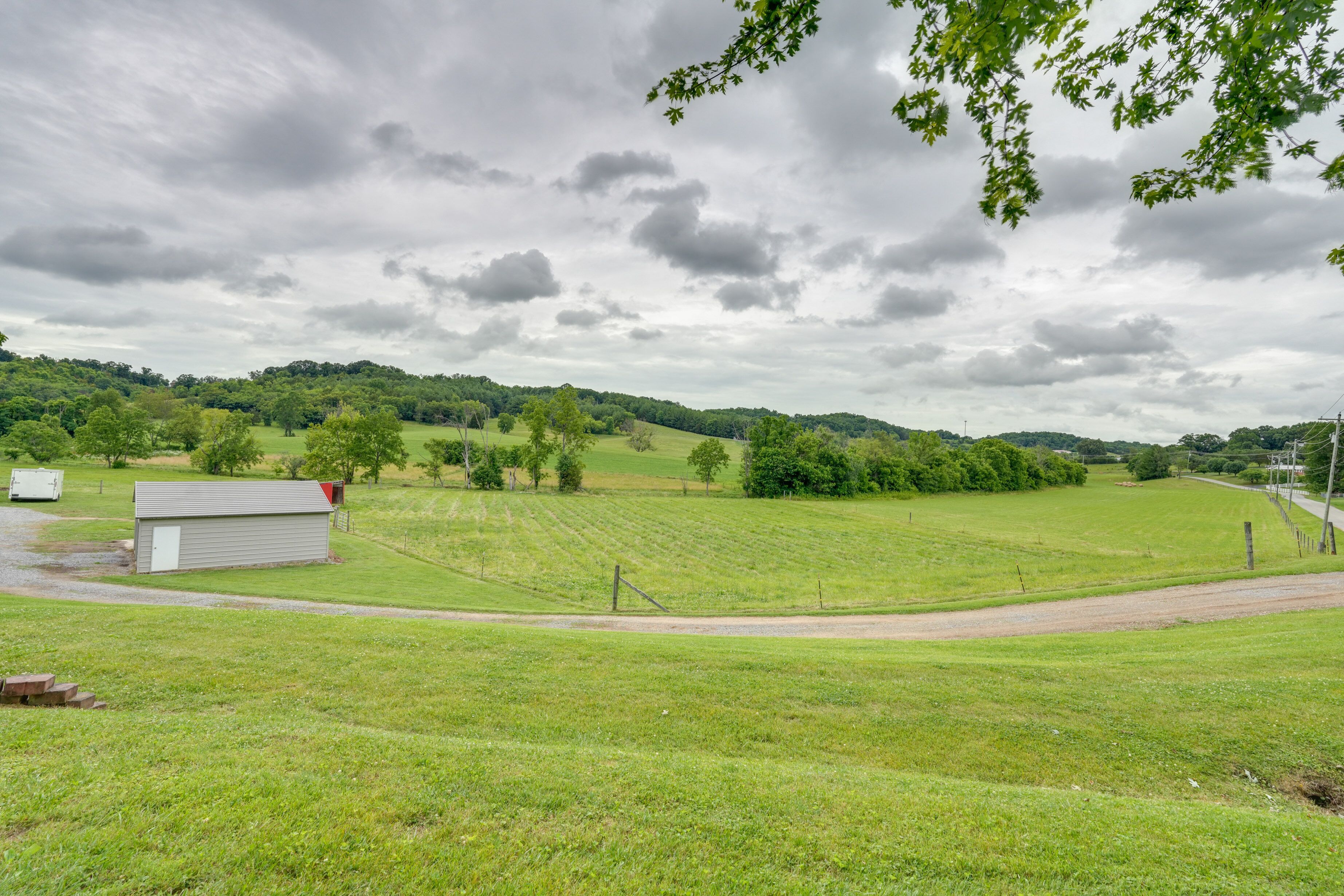 A rural landscape with a small shed, a dirt road, and a grassy field.