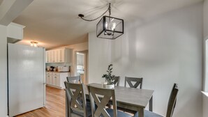 A modern kitchen with wooden cabinets, a dining table with chairs, and a hanging light fixture. - Countryside Hideaway in Greeneville w/ Fire Pit! (Greeneville)