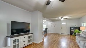 A spacious living room with hardwood floors, a flat-screen TV on a white cabinet, a ceiling fan, and a dining area in the background. - Countryside Hideaway in Greeneville w/ Fire Pit! (Greeneville)