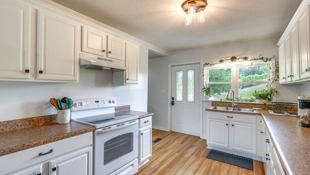 A kitchen with white cabinets, a granite countertop, a stove, and a window with greenery outside. - Countryside Hideaway in Greeneville w/ Fire Pit! (Greeneville)
