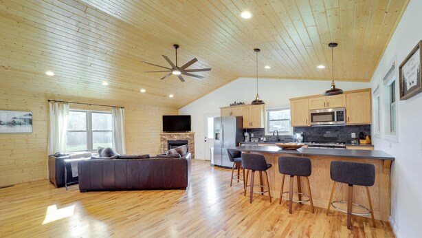 A spacious living area with a wooden ceiling, a fireplace, a large sofa, and a kitchen with a bar area. - Peaceful Purlear Vacation Rental w/ Creek Access! (Purlear)