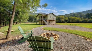 A lodge with a covered deck, a fire pit, and a chair in a natural setting. - Peaceful Purlear Vacation Rental w/ Creek Access! (Purlear)