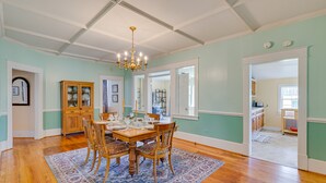Une salle à manger avec une table en bois, des chaises et un lustre. On y trouve un buffet aux portes vitrées et un tapis sur le sol.