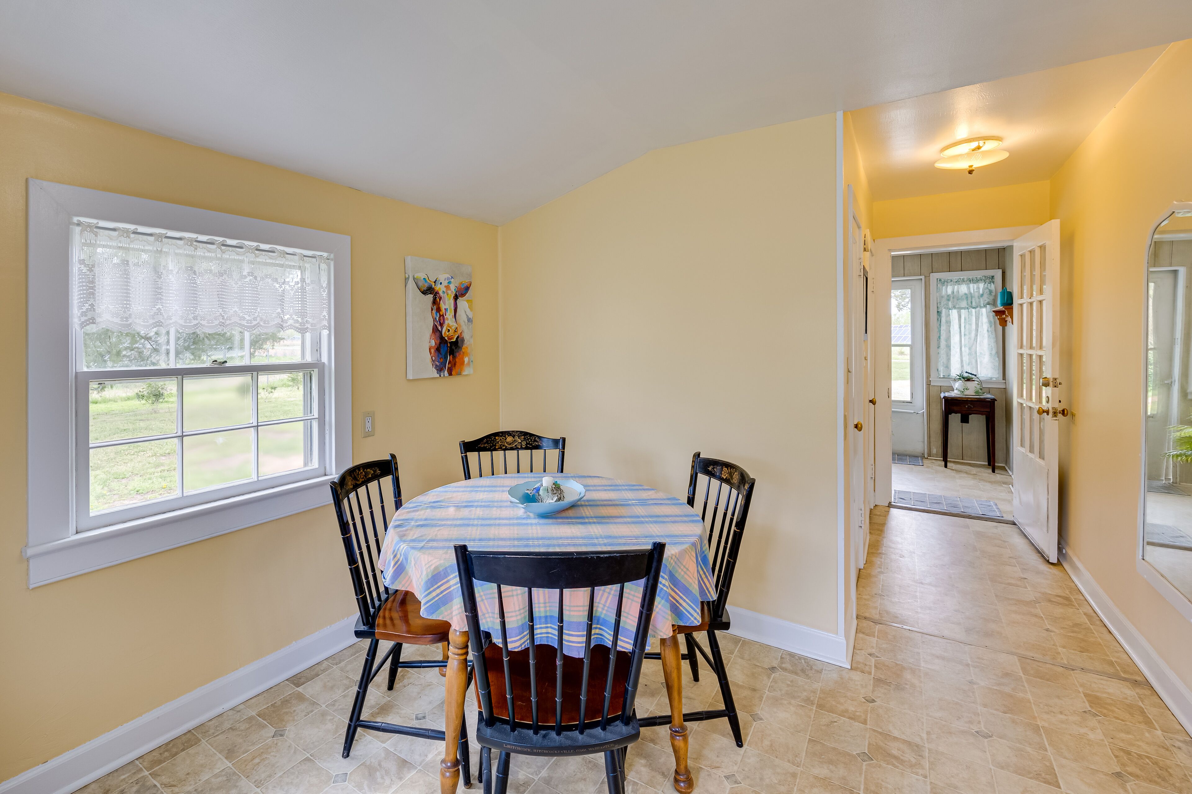 A dining area with a table set for four, chairs, a window with a view, and a door leading to another room.
