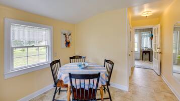A dining area with a table set for four, chairs, a window with a view, and a door leading to another room.