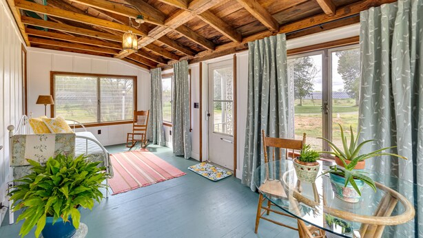 Une pièce avec un plafond en bois, de grandes fenêtres, une table en verre ornée de plantes et une chaise.