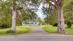 Une maison avec une allée en gravier menant à la porte d’entrée, entourée de grands arbres et d’une pelouse bien entretenue.