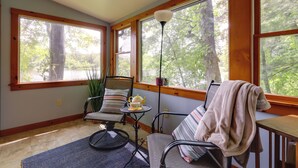 A sunlit room with large windows, a chair, a small table with a teapot, and a floor lamp. - Lakefront Connecticut Retreat Near Uconn (Coventry)