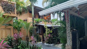 A courtyard with potted plants, a tiled floor, and a building with a tiled facade. - Casa Shangri La (Canoa)