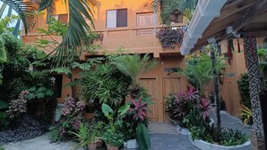 A courtyard with a two-story building, potted plants, and a wooden door. - Casa Shangri La (Canoa)