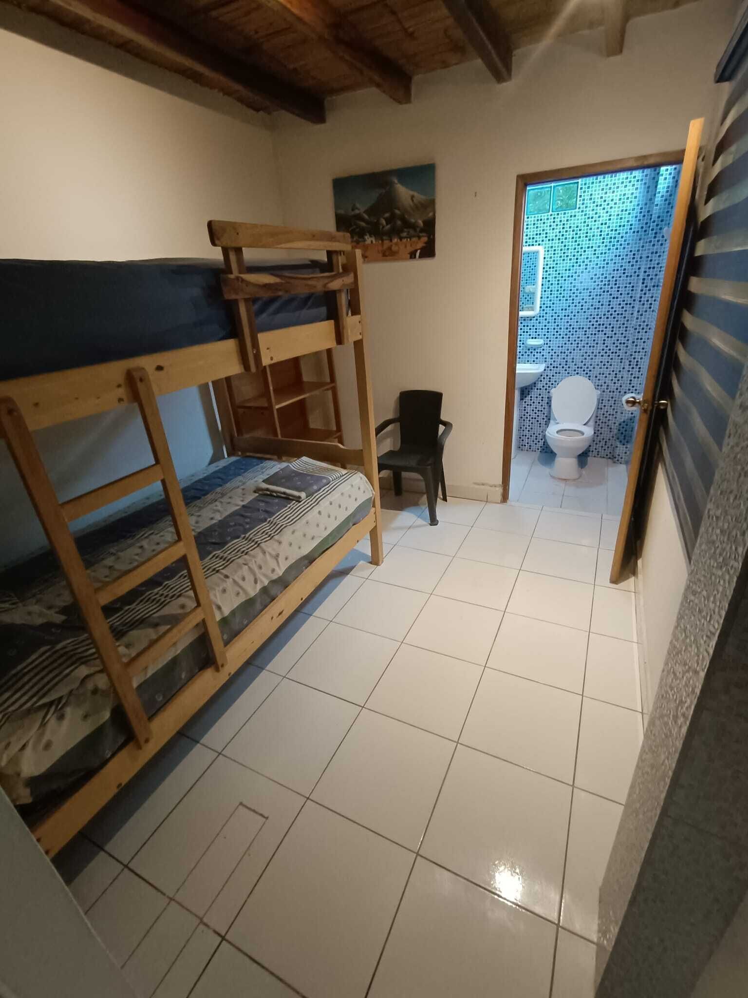 A small, clean room with a bunk bed, a chair, and a toilet.