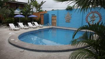 A swimming pool with lounge chairs and umbrellas, surrounded by a blue wall with decorative statues.