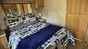 A bedroom with a large bed, wooden cabinets, a mirror, and a door. - Cozy Park Model minutes from many of UPs popular attractions & UTV/ATV Snow Trls (White Pine)
