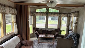 A cozy living area with a brown leather couch, a coffee table, and a ceiling fan. - Cozy Park Model minutes from many of UPs popular attractions & UTV/ATV Snow Trls (White Pine)