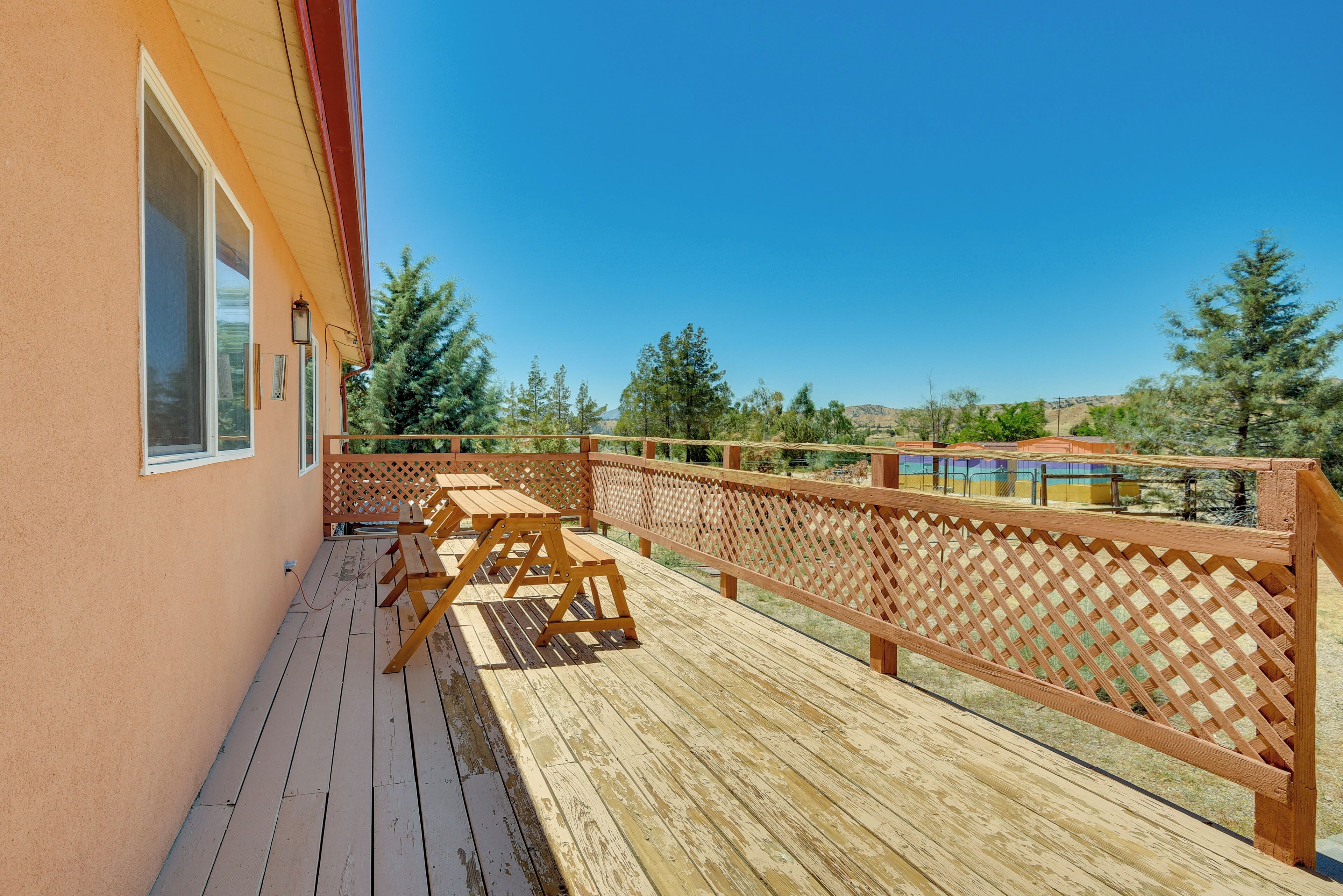 A wooden deck with picnic tables and a lattice railing, overlooking a scenic landscape with trees and hills.