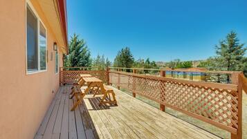 A wooden deck with picnic tables and a lattice railing, overlooking a scenic landscape with trees and hills.