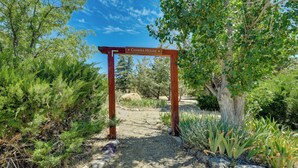 Ein hölzerner Bogen, der mit „Chakra House“ beschriftet ist, führt in einen Gartenbereich mit verschiedenen Pflanzen und Bäumen.