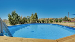 Ein klarer, blauer Swimmingpool mit einer Holzterrasse im Vordergrund, umgeben von Bäumen und Hügeln im Hintergrund.