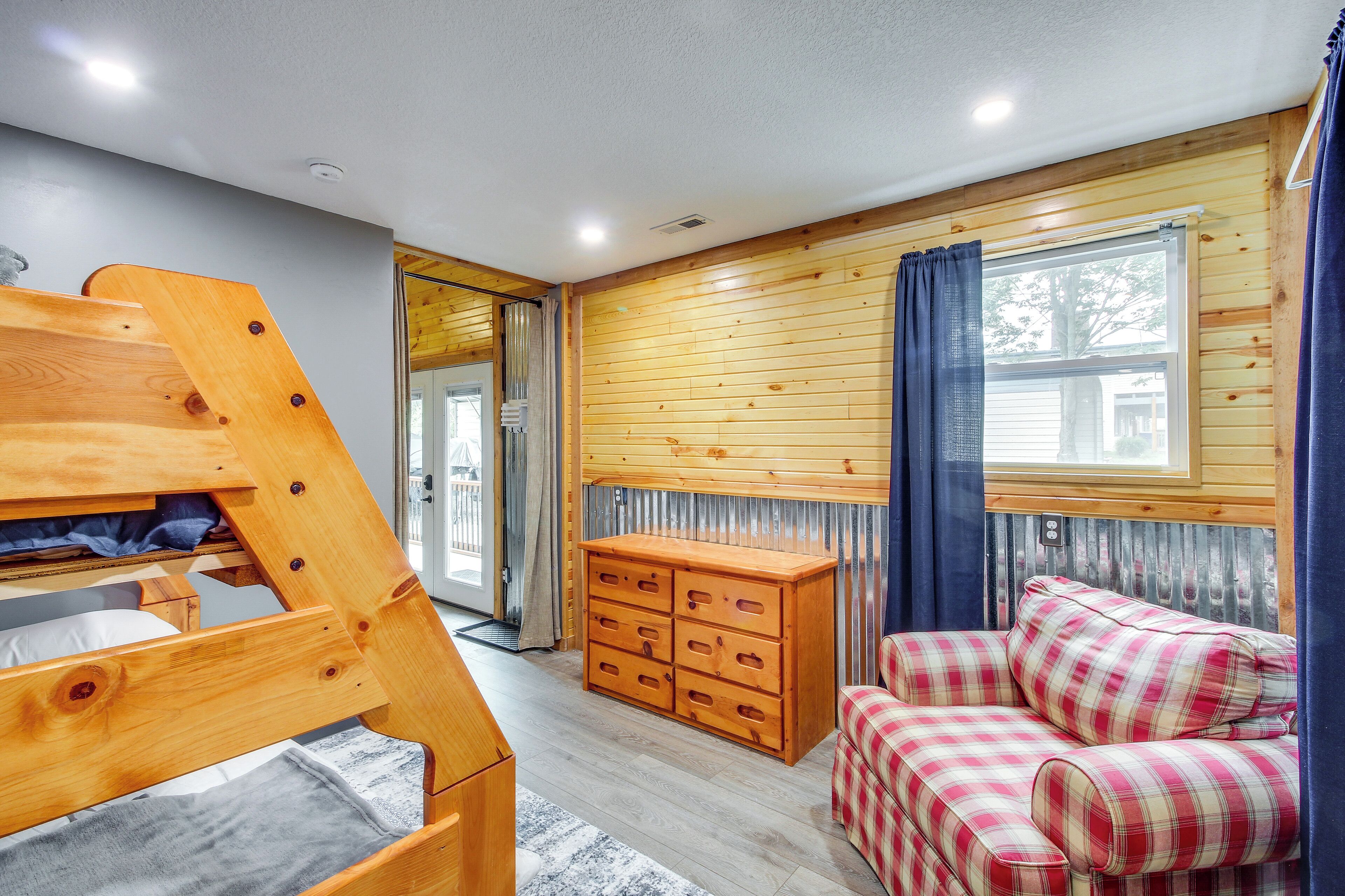 A room with a bunk bed, a plaid sofa, a wooden dresser, and a window with curtains.