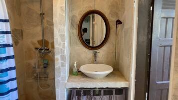 A bathroom with a stone wall, a round mirror, a white sink, and a shower.