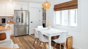 Een moderne keuken met witte kasten, een roestvrijstalen koelkast en een eethoek met een witte tafel en stoelen.