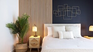 Een moderne slaapkamer met een groot bed, een potplant, een nachtkastje en een kunstwerk aan de muur.