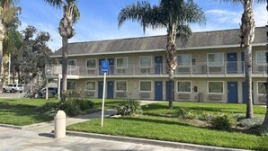 Un motel à plusieurs étages, doté d’un parking, d’un panneau indiquant qu’il est accessible aux personnes handicapées et de palmiers.