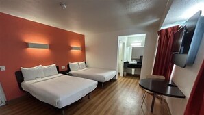 Une chambre d’hôtel avec deux lits, une petite table, une télévision et une salle de bain visible à travers une porte ouverte.