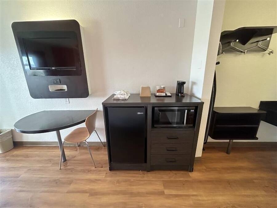 A compact kitchenette with a microwave, a small refrigerator, a coffee maker, and a flat-screen TV mounted on the wall.