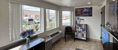 A reception area with a counter, a chair, a bulletin board, and a window with a view of parked cars outside.