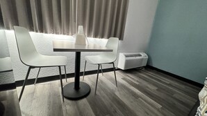 Ein modernes Zimmer mit Holzboden, einem weißen Tisch mit vier Stühlen, einer weißen Klimaanlage und einem Fenster mit Vorhängen.